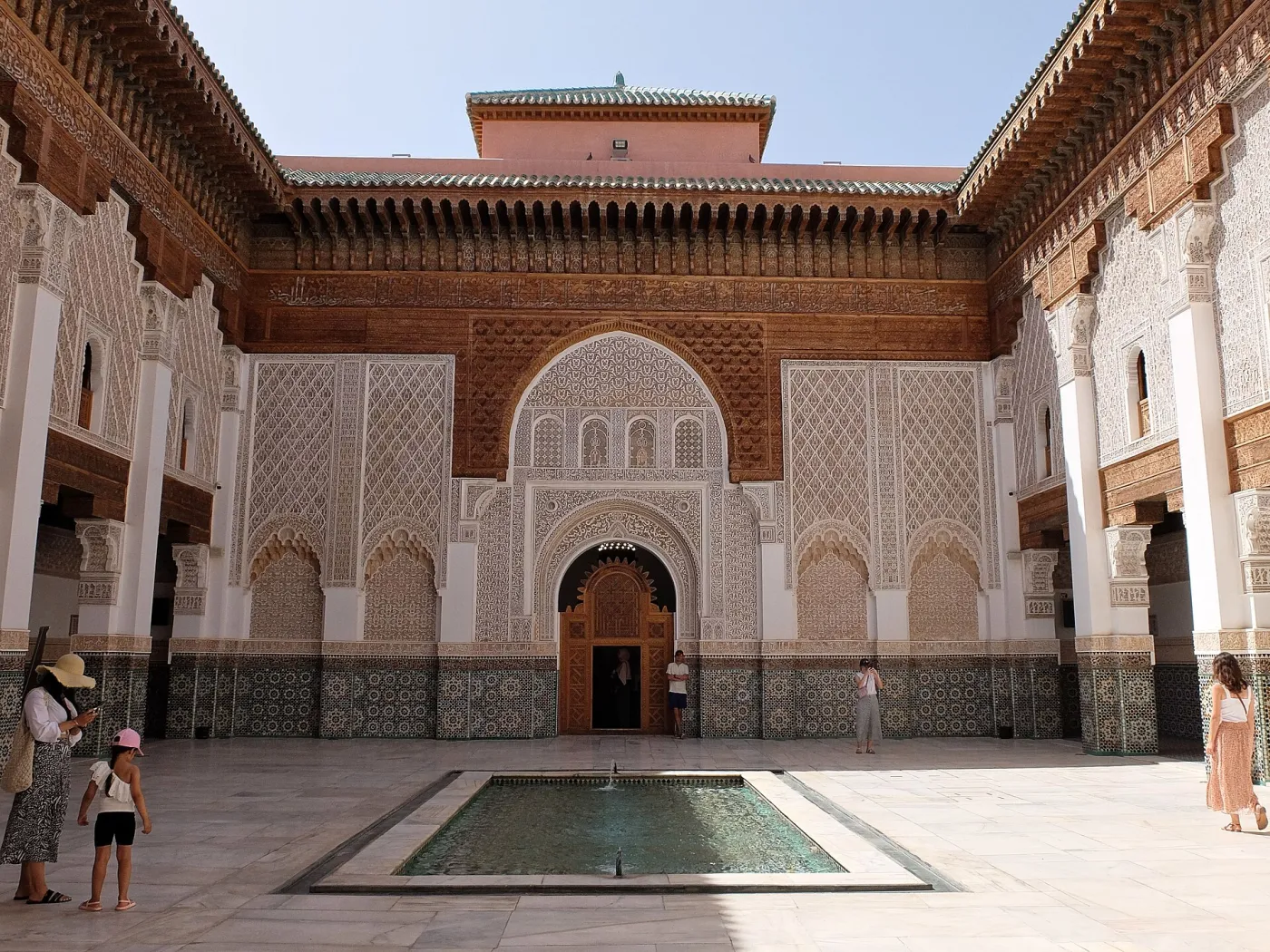 The marble courtyard and central pool of the Ben Youssef Madrasa in Marrakech, framed by carved cedar and stucco arches