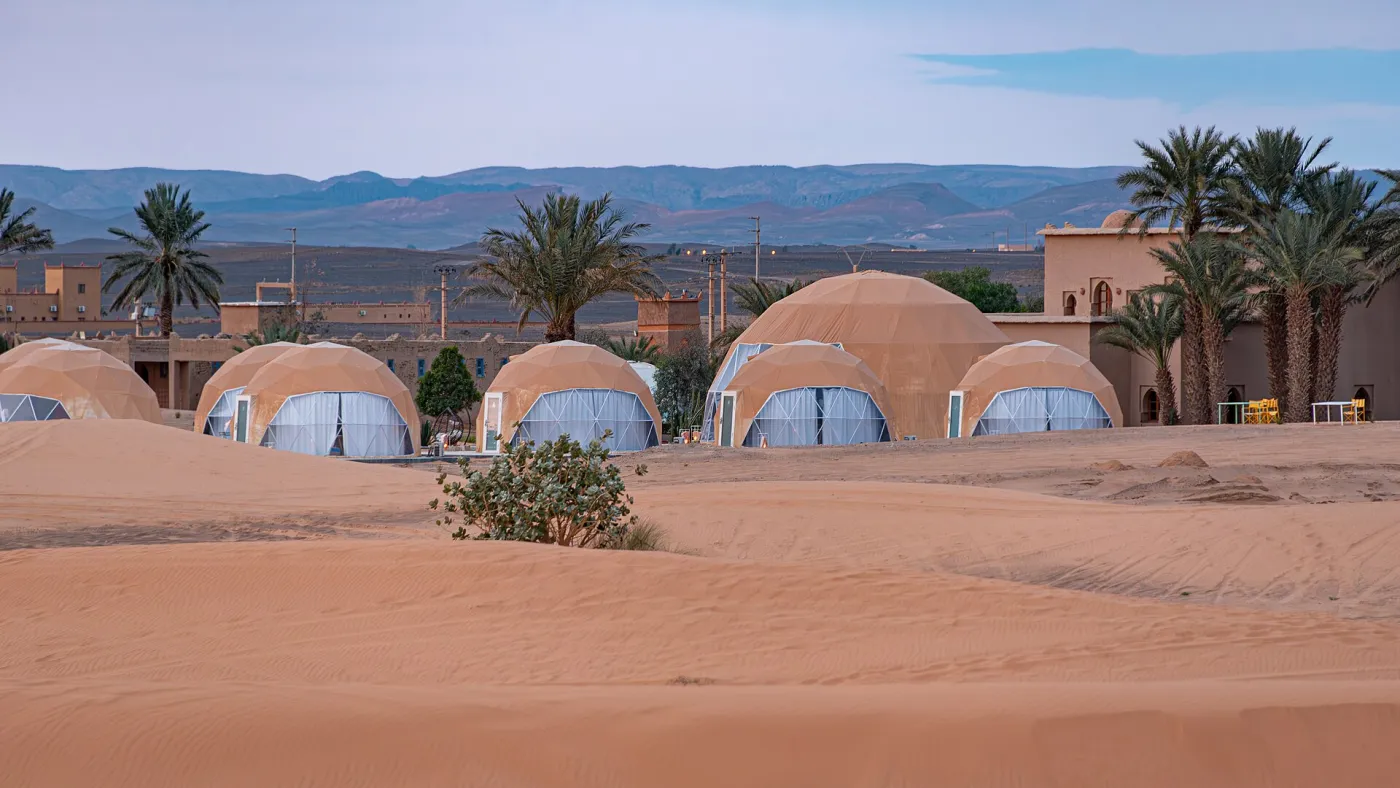 Domed desert camp among palm trees at the edge of the Erg Chebbi dunes