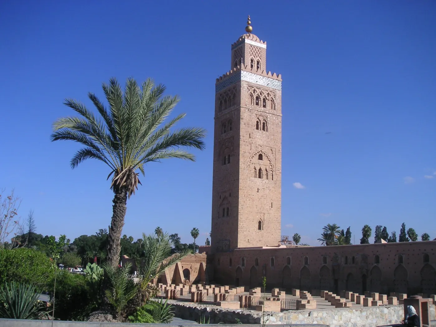 The 77-metre Koutoubia Mosque minaret in Marrakech against a clear blue sky, palm trees and rose gardens in the foreground