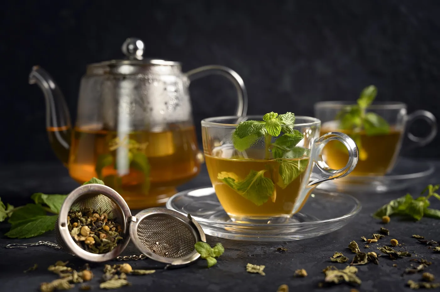 Silver teapot pouring fresh mint tea into small decorated glasses on a brass tray in a Moroccan café