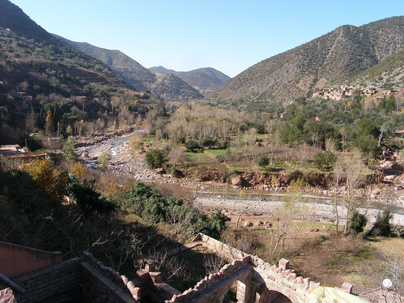 Terraced Berber village of red earth houses above the green Ourika Valley with the High Atlas peaks behind