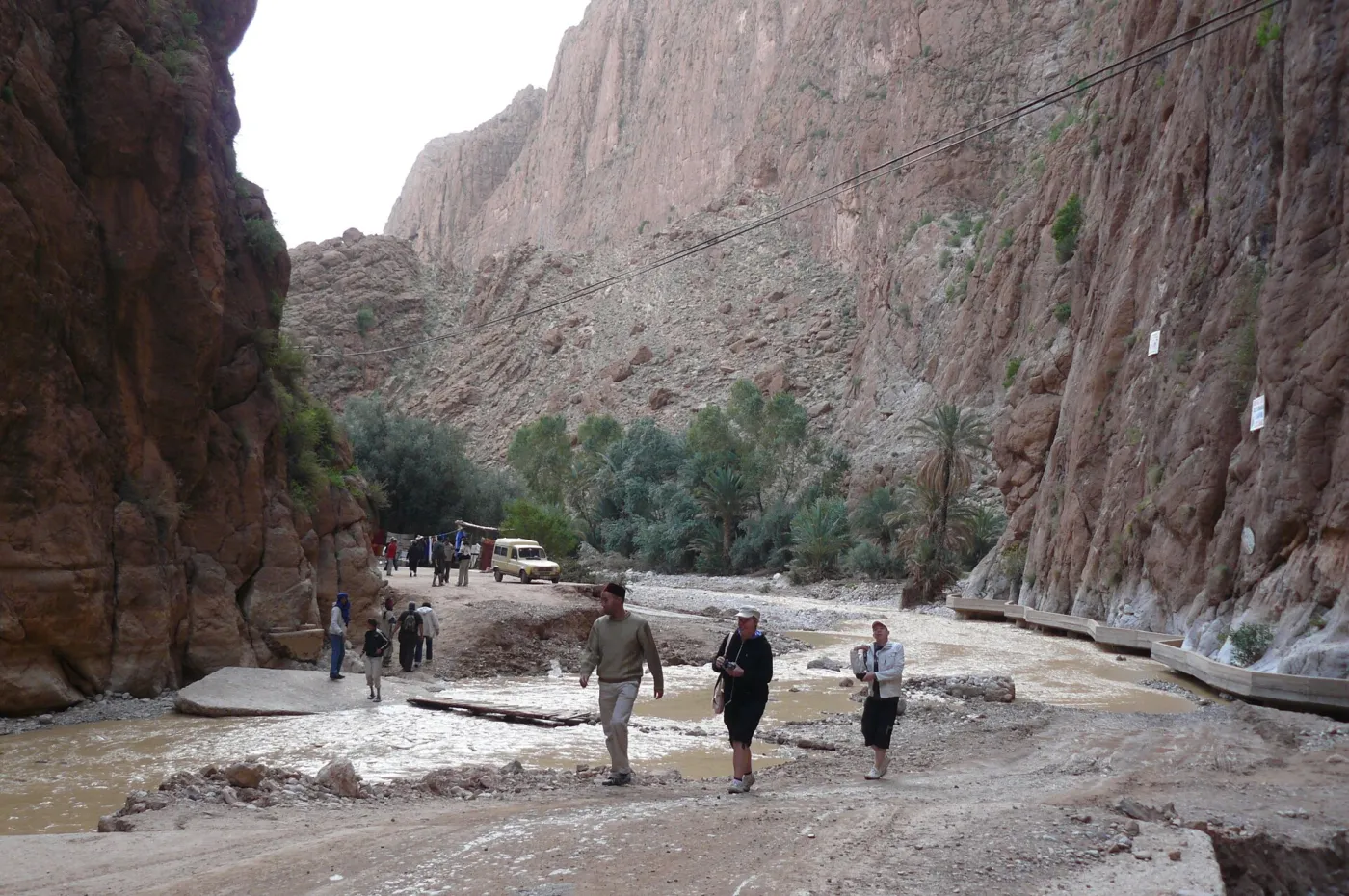 Sheer orange limestone walls of Todra Gorge towering over a shallow river and a narrow road near Tinghir